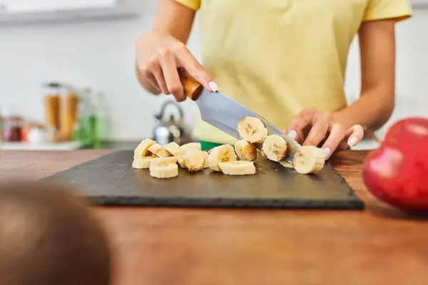 Vista parziale di giovane donna che taglia banana matura mentre cucina pasto vegetariano in cucina a casa — Foto stock