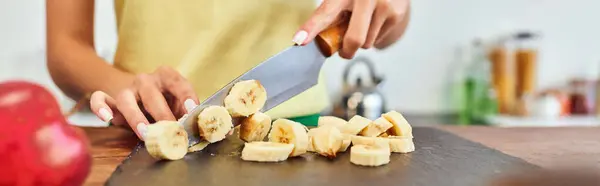 Vista cortada da mulher cortando banana fresca madura na cozinha, conceito de dietas à base de plantas, banner — Fotografia de Stock