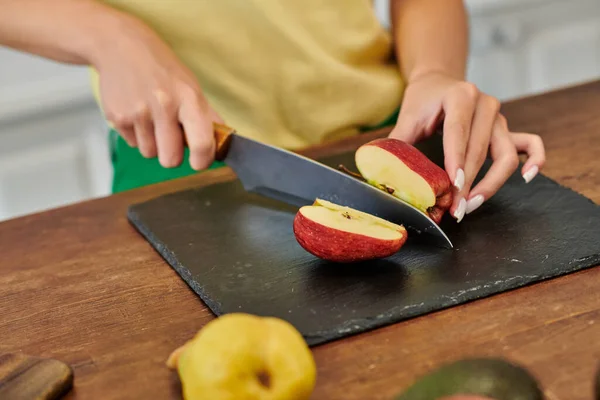 Частичный вид женщины, режущей спелое яблоко на доске рядом с грушей, приготовление вегетарианской еды — стоковое фото