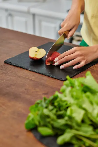 Vista ritagliata della donna che taglia mela vicino alla lattuga fresca sul piano di lavoro in cucina, dieta incentrata sulle piante — Foto stock