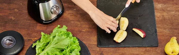 Обрезанная вегетарианка режет яблоко рядом с электрическим блендером и свежим салатом, горизонтальным баннером — стоковое фото
