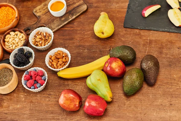Вид зверху на свіжі фрукти і асортимент горіхів біля обробних дощок на дерев'яному столі, вегетаріанська дієта — стокове фото
