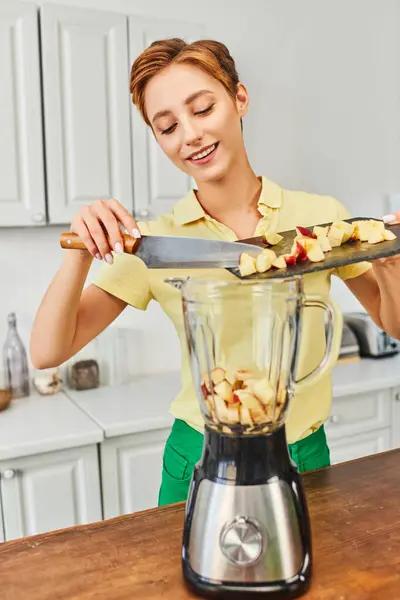 Femme heureuse avec pomme hachée sur planche à découper près d'un mélangeur électrique, concept de régimes à base de plantes — Photo de stock