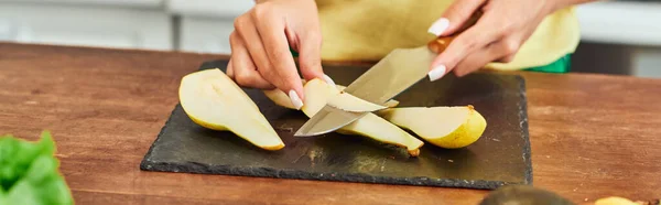 Vista cortada de mulher vegetariana cortando pêra madura em tábua de corte na cozinha, bandeira horizontal — Fotografia de Stock