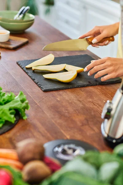 Частковий вигляд вегетаріанки з ножем біля стиглої нарізаної груші на дошці на кухні — стокове фото