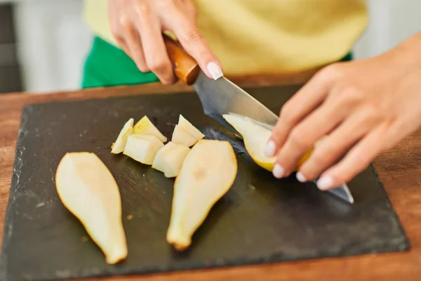 Vue recadrée de femme coupant poire fraîche mûre sur planche à découper, concept culinaire à base de plantes — Photo de stock