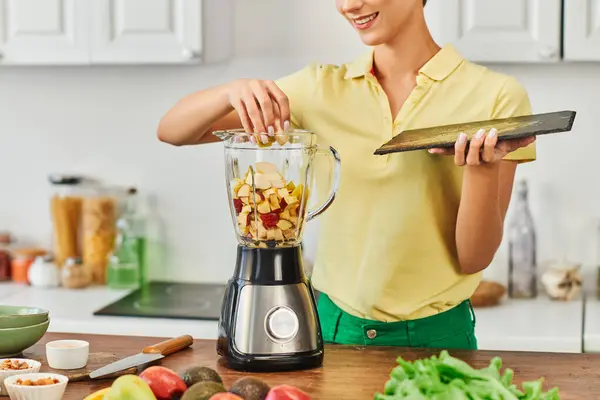 Vue recadrée de joyeuse femme mélangeant des fruits hachés dans un mélangeur électrique, délicieuse recette végétarienne — Photo de stock