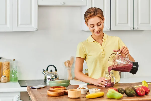 Pleased woman pouring delicious smoothie from electric blender into mason jar, plant-based diet — Stock Photo