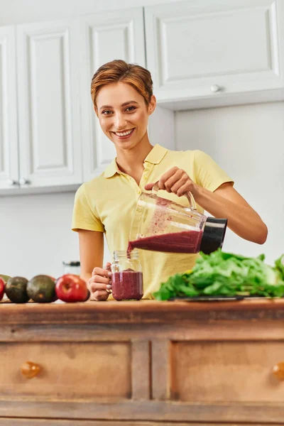 Vegetarian culinary delight, happy young woman pouring fresh smoothie from blender into mason jar — Stock Photo