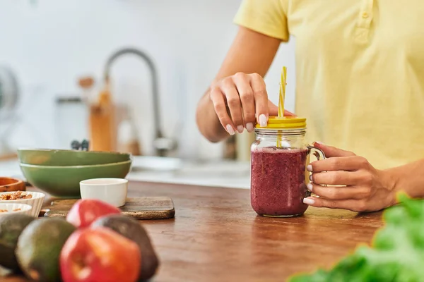 Cropped view of woman near mason jar with delicious plant-based smoothie near blurred fresh fruits — Stock Photo