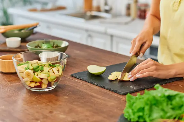 Обрізаний вид на жінку, що ріже стиглу грушу біля миски з фруктовим салатом, здорове вегетаріанське харчування — стокове фото