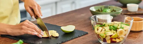 Частковий вид на вегетаріанку, що ріже грушу біля миски зі свіжим фруктовим салатом, горизонтальний банер — стокове фото