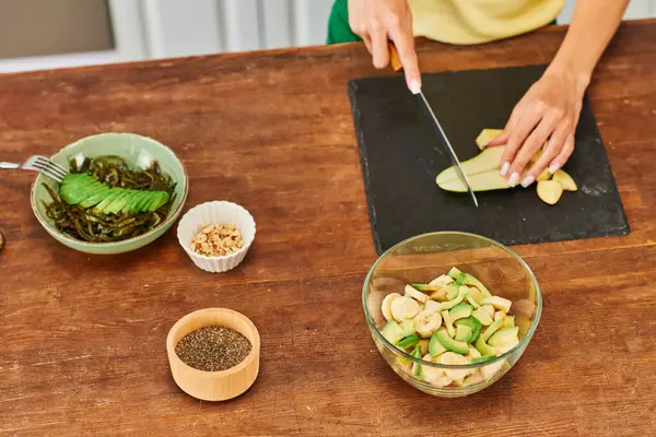 Vista ritagliata di donna taglio pera vicino a diverse insalate con frutta e alghe, dieta vegetariana — Foto stock