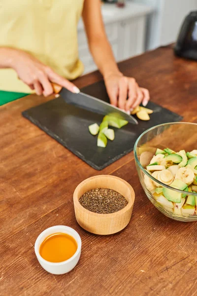 Cropped woman cutting fresh fruits while preparing vegetarian salad near honey and sesame seeds — Stock Photo