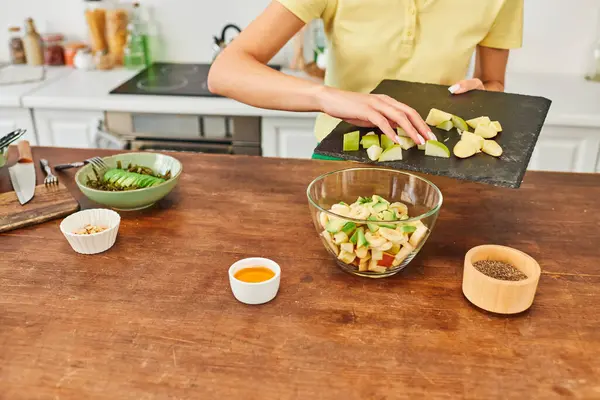 Donna ritagliata tenendo tagliere con frutta tritata durante la preparazione di insalata vegetariana a casa — Foto stock