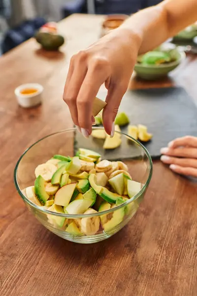 Частковий вигляд жінки біля миски зі свіжими подрібненими фруктами, смачний рецепт вегетаріанського салату — стокове фото