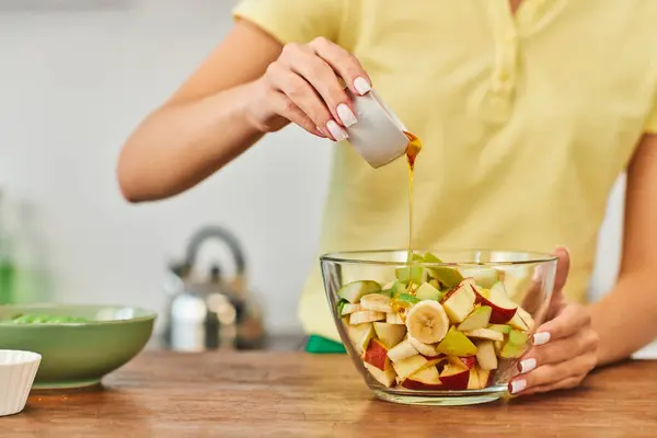 Cropped view of woman pouring honey into bowl with chopped fruits, wholesome vegetarian salad — Stock Photo