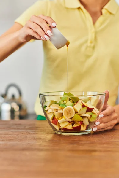 Cropped view of woman pouring honey on fresh fruit salad in glass bowl, delicious plant-based diet — Stock Photo
