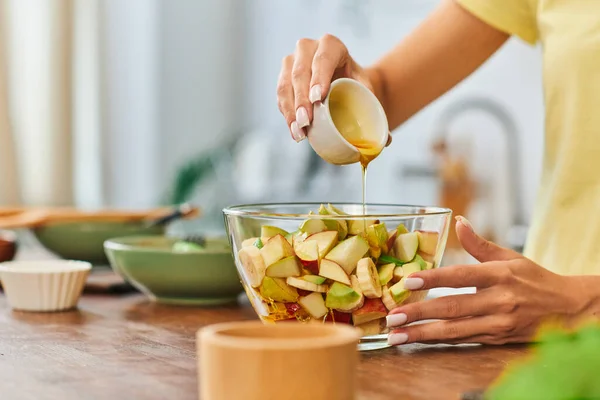 Частичный вид женщины, наливающей мед на здоровый фруктовый салат в стеклянную миску, диета, ориентированная на растения — стоковое фото