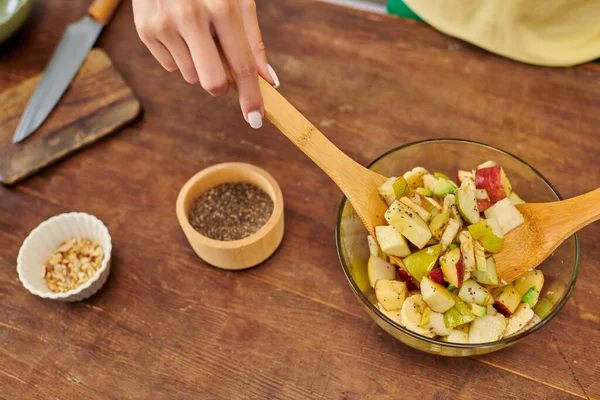 Abgeschnittene Ansicht einer Frau, die Obstsalat in der Nähe von Sesam und Nüssen mixt, leckeres vegetarisches Rezept — Stockfoto
