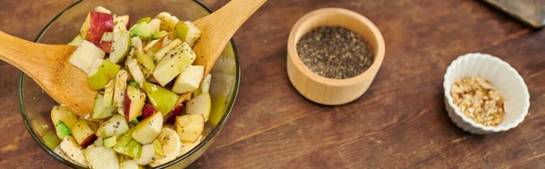 Tigela de vidro com salada de frutas vegetarianas e espátulas de madeira perto de sementes de gergelim e nozes, banner — Fotografia de Stock