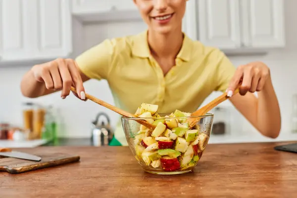 Partial view of woman mixing fresh fruit salad with wooden spatulas in kitchen, vegetarian diet — Stock Photo