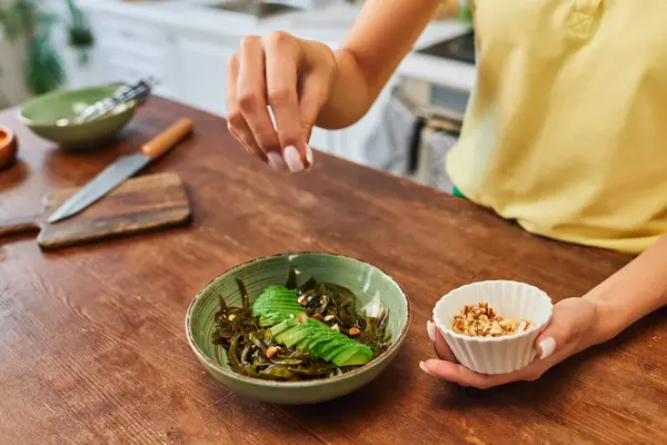 Femme cultivée ajoutant des noix dans la salade végétarienne avec des algues et de l'avocat tranché, régime à base de plantes — Photo de stock