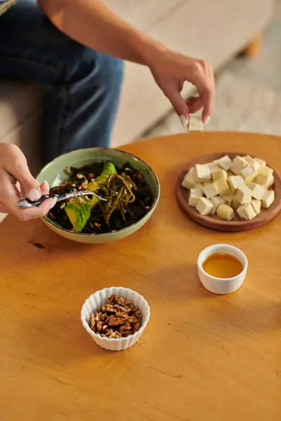 Обрізана жінка біля вегетаріанського салату на рослинній основі і сиру тофу з оливковою олією і волоськими горіхами на столі — стокове фото