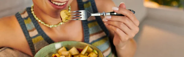 Vista cortada de mulher vegetariana comendo deliciosa salada de frutas para lanche à noite na sala de estar, banner — Fotografia de Stock