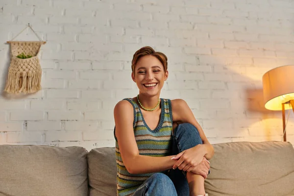 Carefree woman looking at camera while sitting on cozy couch in modern living room at home — Stock Photo