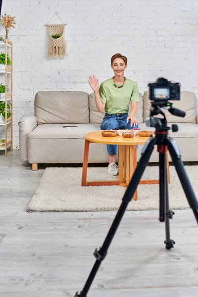 Happy young woman waving hand in front of digital camera while starting vegetarian video blog — Stock Photo