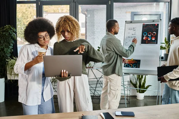 Zwei Frauen, die auf Laptop schauen, während ihre männlichen Freunde an Grafiken auf Hintergrund, Geschäft arbeiten — Stockfoto