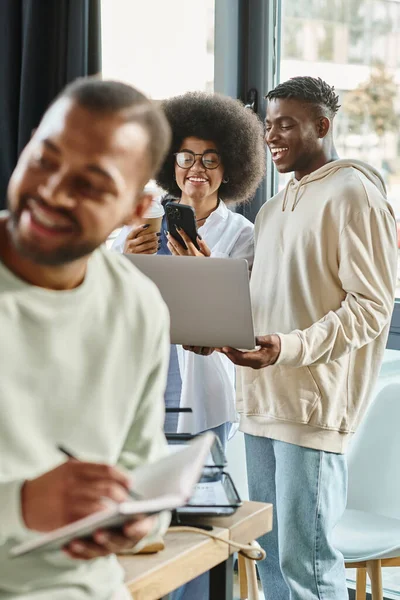 Plano vertical del hombre americano africano sonriente que trabaja con sus amigos en el telón de fondo, concepto de negocio - foto de stock