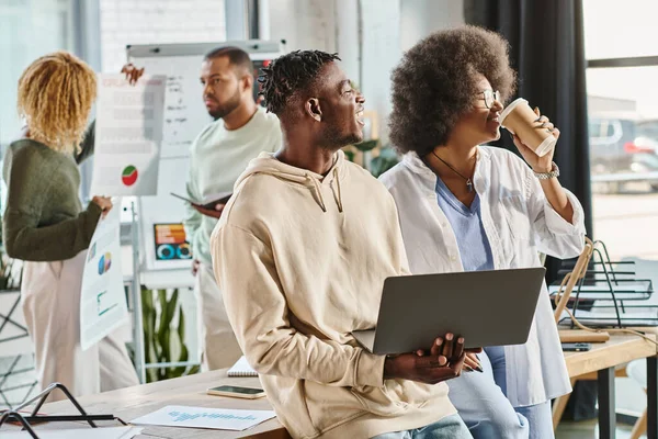 Freudige Teammitglieder mit Kaffee und Laptop in der Hand mit ihren Freunden vor dem Hintergrund, Arbeitsprozess — Stockfoto