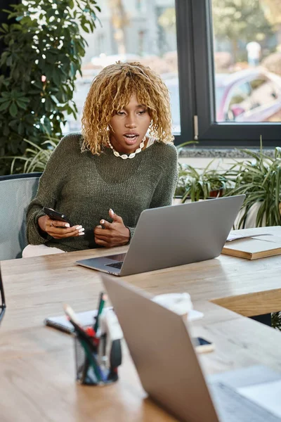 Schöne Frau mit lockigem Haar schaut überrascht auf Laptop, leicht geöffneter Mund, Arbeitsprozess — Stockfoto