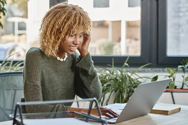 Donna allegra attraente con bretelle guardando il suo computer portatile e sorridendo sinceramente, processo di lavoro — Foto stock