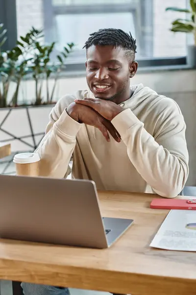 Homme gai en tenue décontractée regardant ordinateur portable et souriant avec les mains sous le menton, processus de travail — Photo de stock