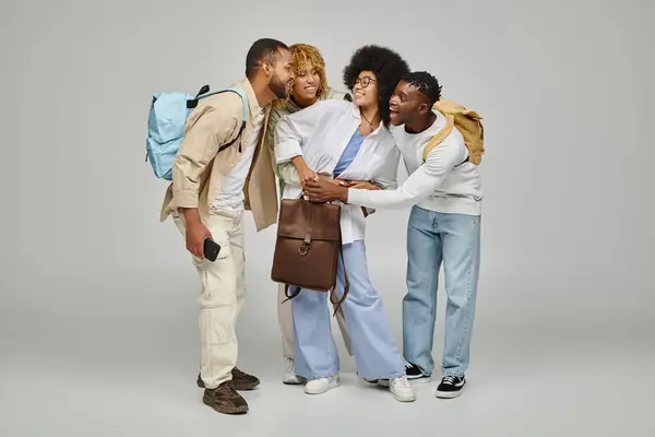 Alegres amigos afroamericanos en atuendos casuales sonriendo y sosteniendo mochilas, estilo de vida estudiantil - foto de stock