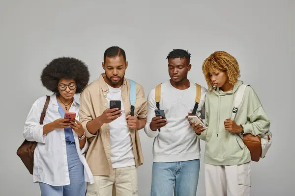 Gruppe von Freunden in lässigen Outfits mit Rucksäcken, die auf ihre Mobiltelefone schauen und Konzept studieren — Stockfoto