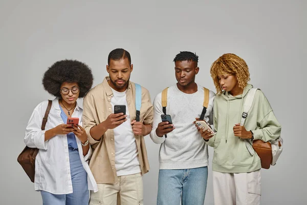 Group of friends in casual outfits with backpacks looking at their mobile phones, studying concept — Stock Photo