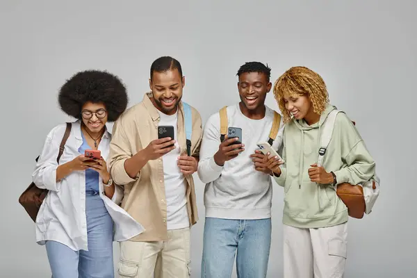 Jovens amigos alegres em desgaste urbano rua olhando para seus telefones e sorrindo alegremente, estudantes — Fotografia de Stock