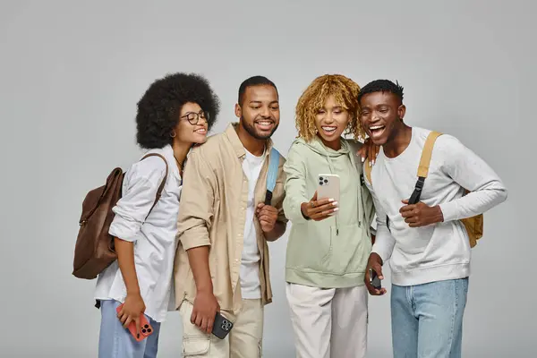 Good looking friends in casual outfits with backpacks looking at phone smiling happily, students — Stock Photo