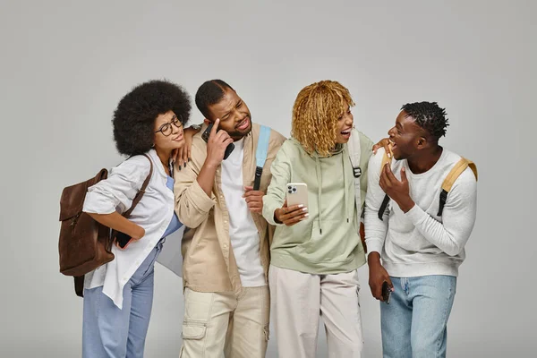 Confuso jovem grupo de amigos em trajes urbanos com mochilas olhando para o telefone celular, estudante — Fotografia de Stock
