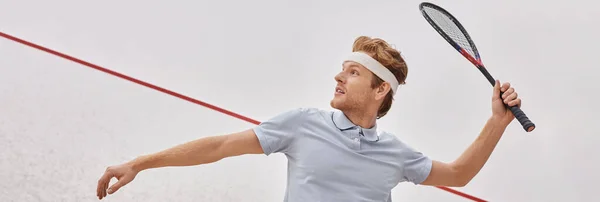 Homme rousse en vêtements de sport et bandeau tenant la raquette et jouant à la courge à l'intérieur de la cour, bannière — Photo de stock