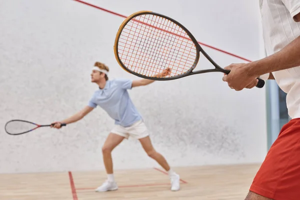 Focus sur l'homme afro-américain en vêtements de sport jouer avec un ami rousse à l'intérieur du court de squash — Photo de stock