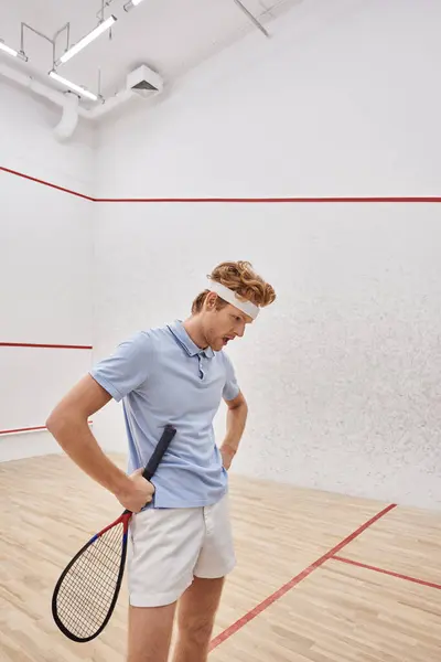 Erschöpfter Mann mit Stirnband und Sportkleidung atmet nach Squash-Spiel im Innenhof schwer — Stockfoto
