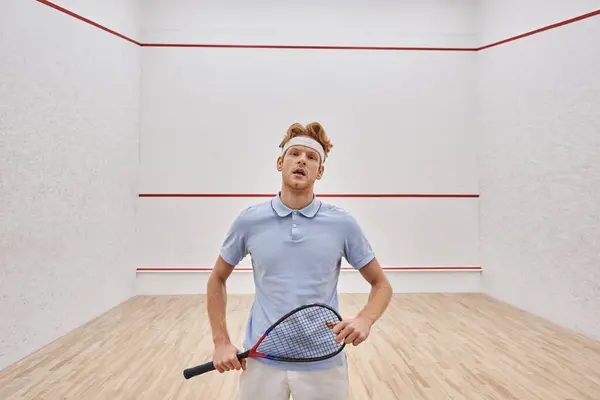 Tired man in headband and sportswear breathing heavily after playing squash inside of court — Stock Photo