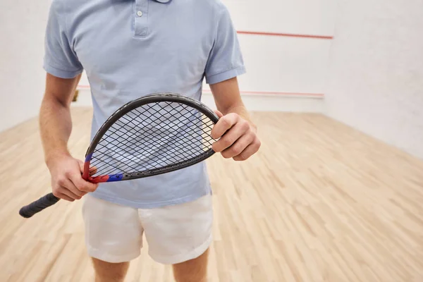 Vista recortada del hombre en ropa deportiva celebración de raqueta de squash y de pie dentro de la cancha cubierta — Stock Photo