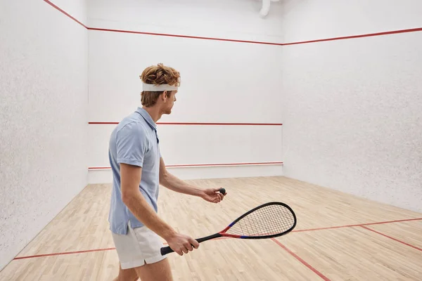 Sportif rousse en tenue de sport tenant balle de squash et raquette tout en jouant à l'intérieur du court — Photo de stock