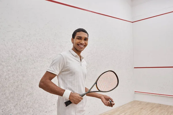 Happy african american man in active wear holding squash ball and racquet while playing in court — Stock Photo
